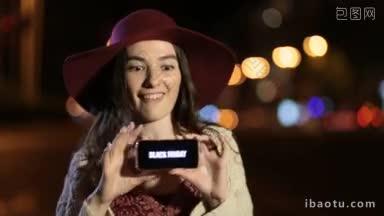 网上购物的女人拿着智能手机，屏幕上有黑色星期五的销售广告文字，在夜晚城市街灯的彩色散景